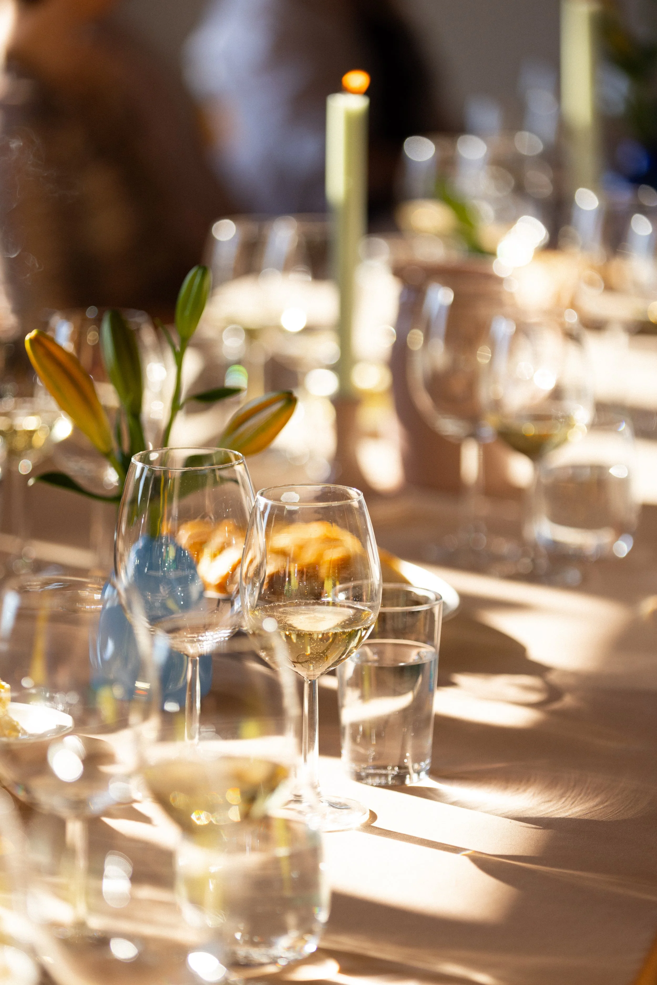Glas med hvitvin på en lys borddekking med blomster og lysestaker