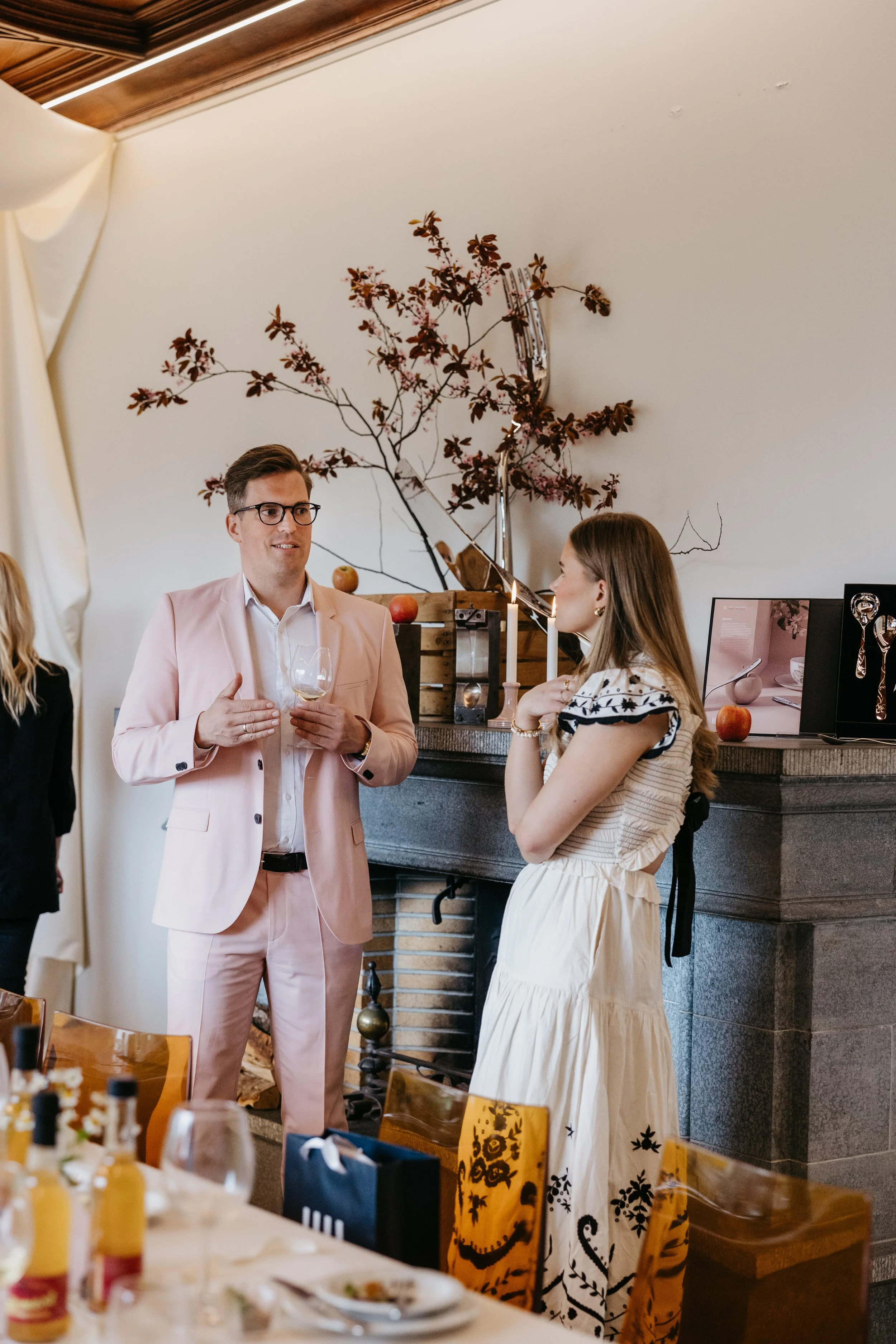 Mann og kvinne snakker under en sammenkomst i et rom med peis og dekorative gjenstander.