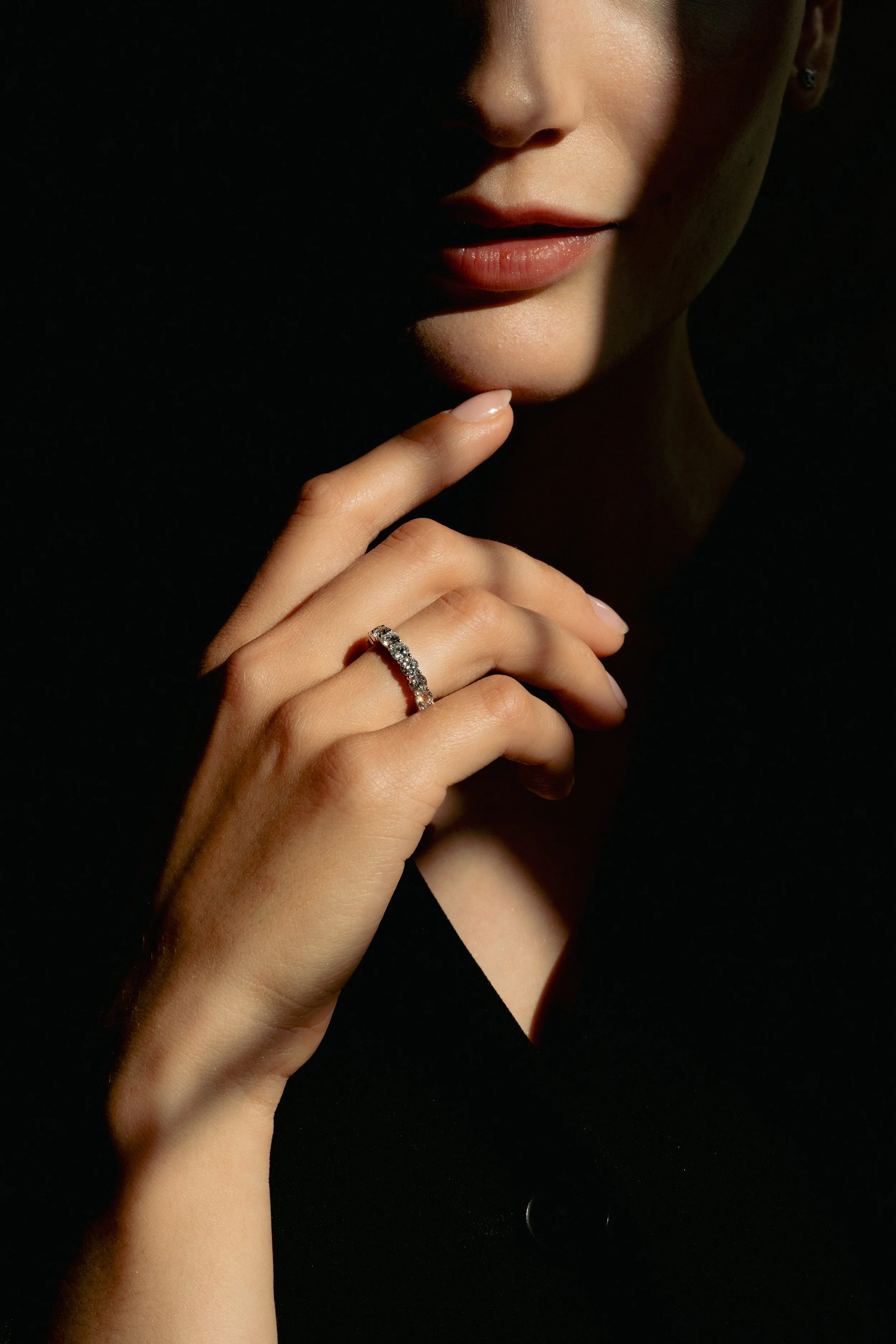 Nærbilde av en kvinnes hånd med en diamant ring, med fokus på leppen og ansiktet, fotografert i lav belysning.