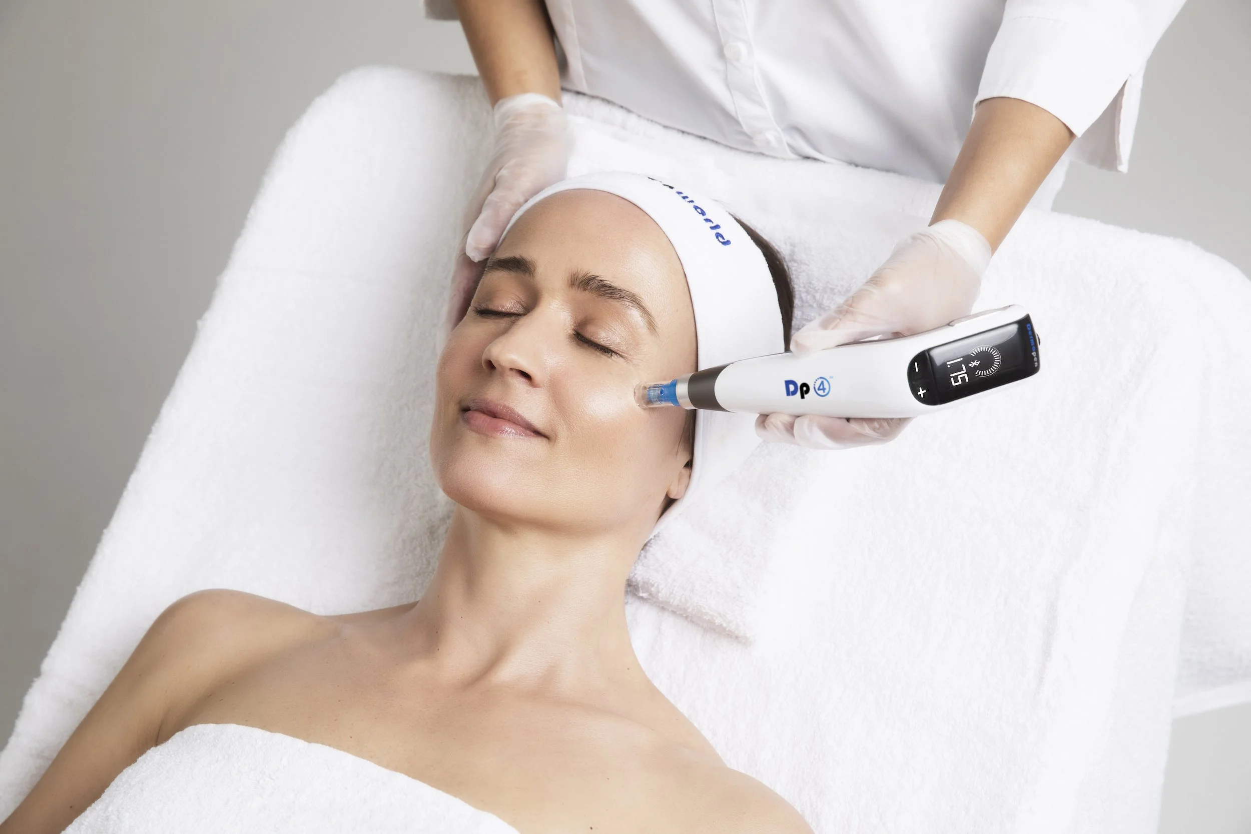 A woman lying on a treatment table receiving a facial procedure from a professional using a skincare device.