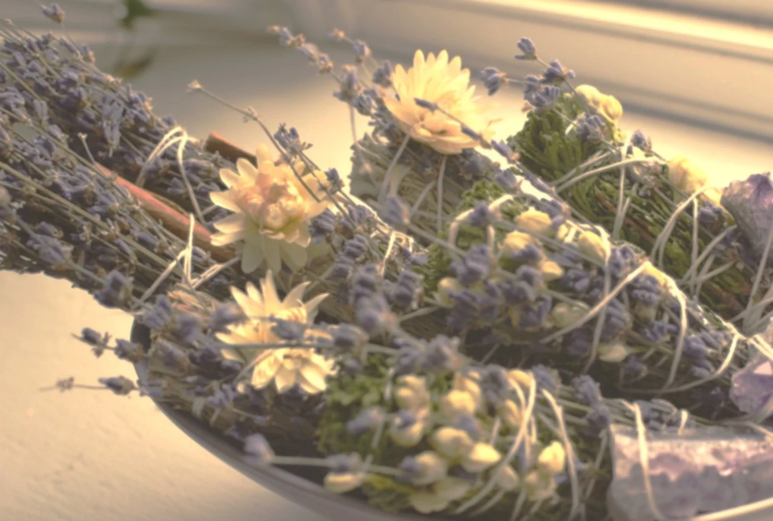 A floral arrangement with white and purple flowers, possibly lavender and roses, placed in a shallow bowl, illuminated by soft, warm light.