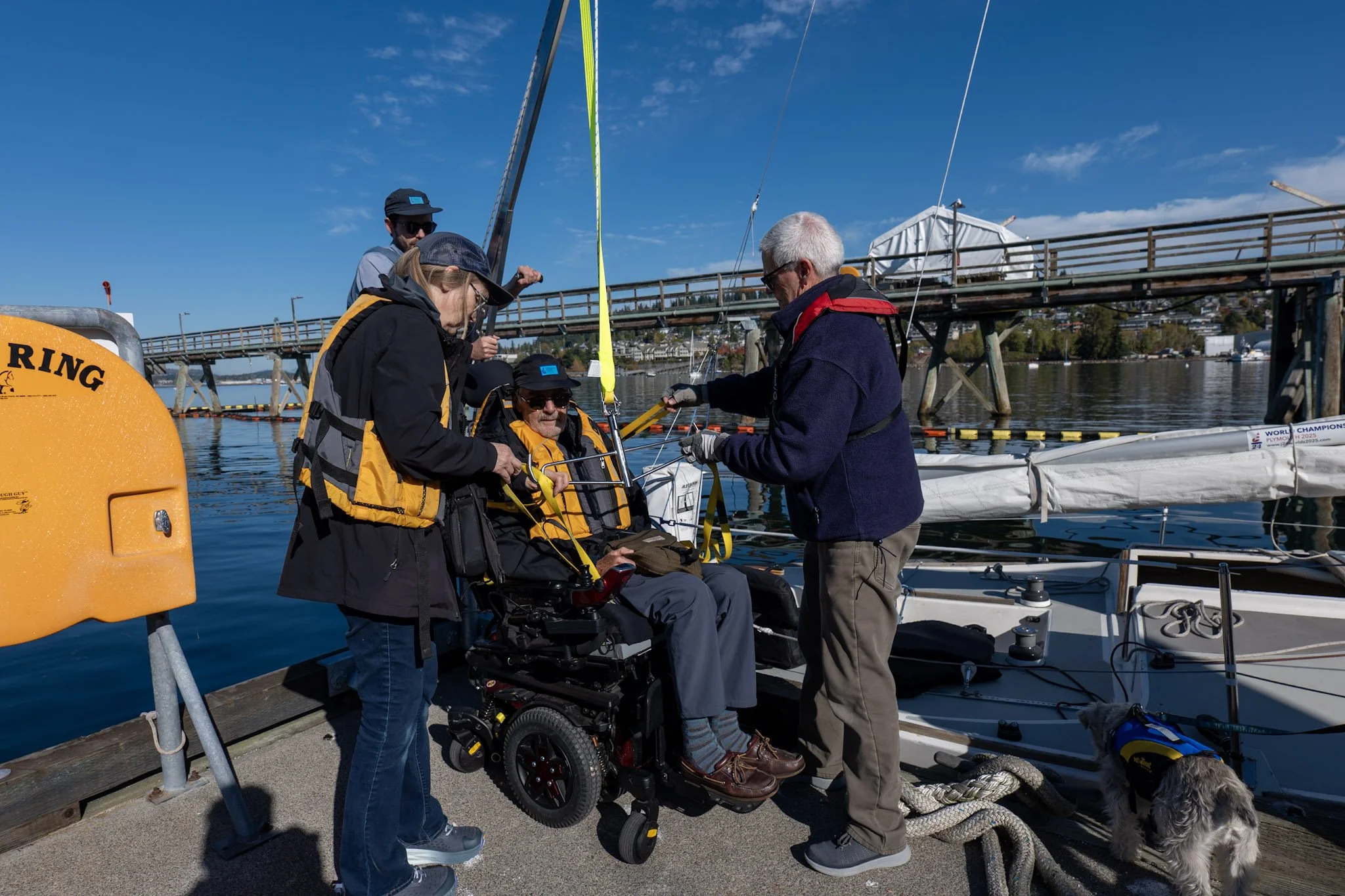 Volunteers help a participant use the adaptive lift to get from the dock into a sailboat.