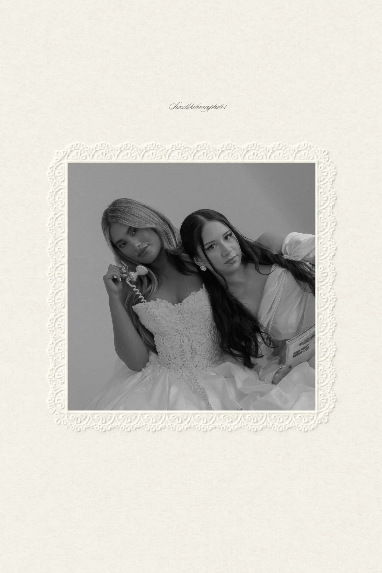 Black and white photo of two women in elegant dresses, one holding a vintage telephone, both looking at the camera, framed with lace border.