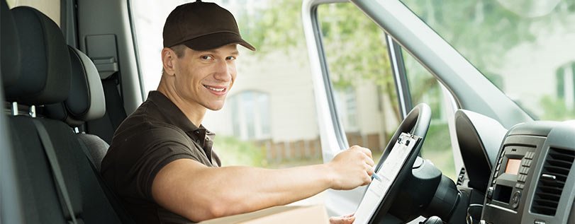 A delivery driver sitting in the driver's seat of a van, smiling at the camera, with a tablet in hand.