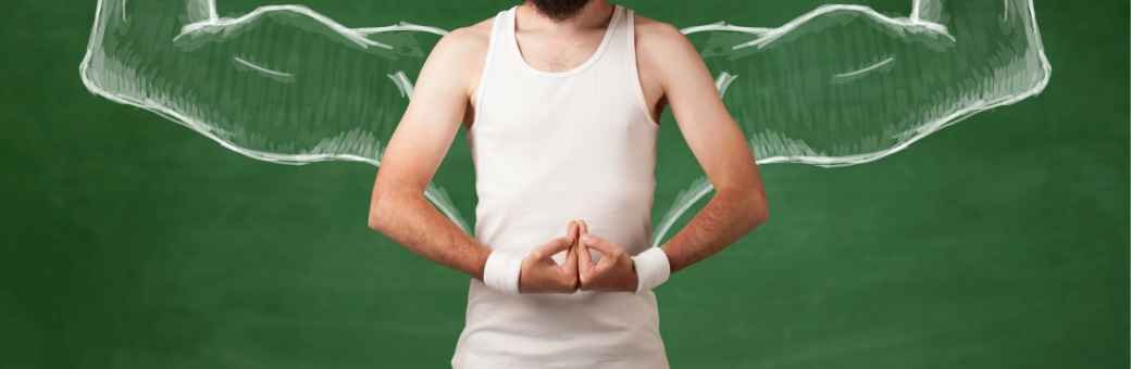 Man in white tank with thin arms in front of chalkboard with chalk drawing of flexing biceps.