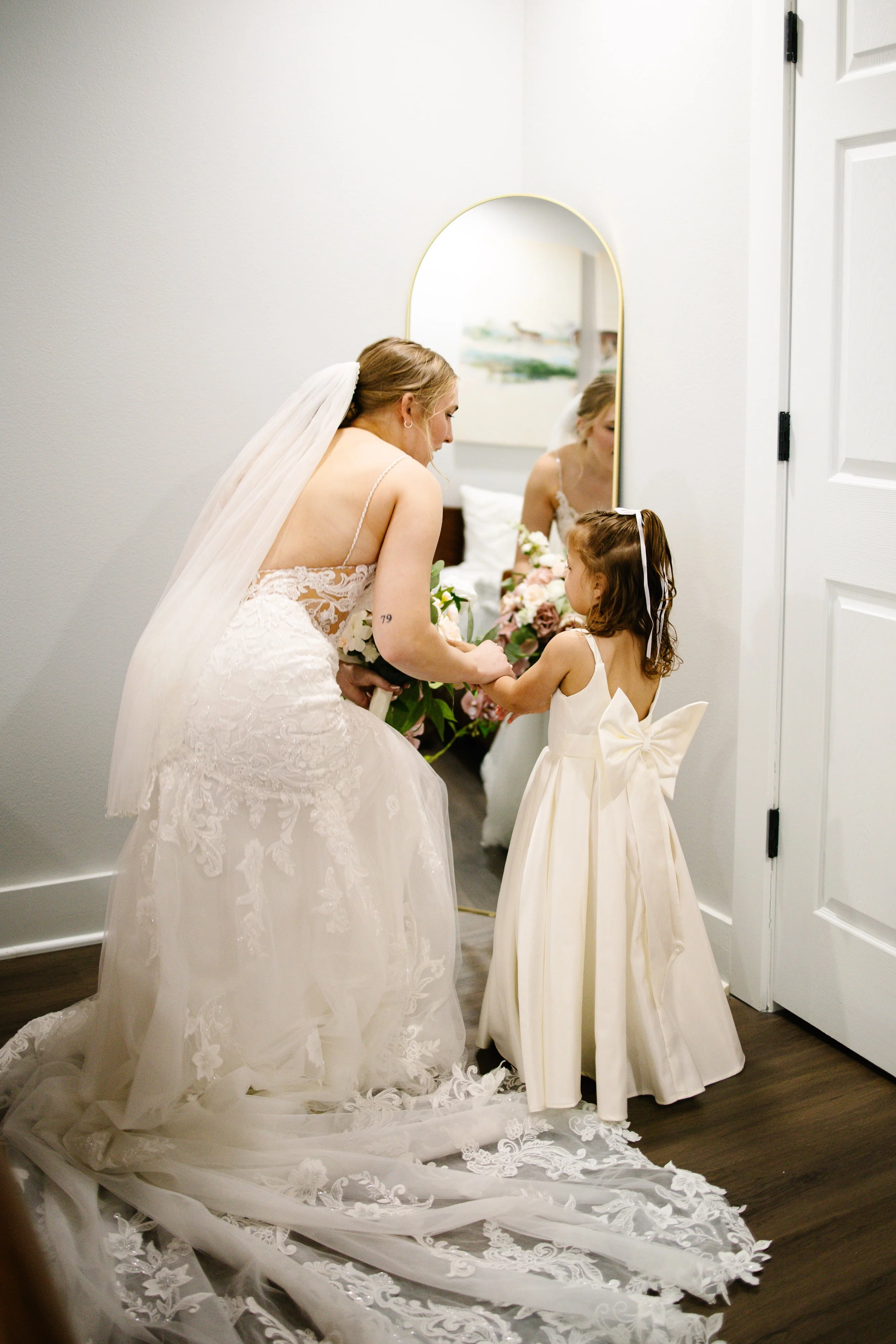 Bride crouching beside flower girl during intimate wedding getting ready moments