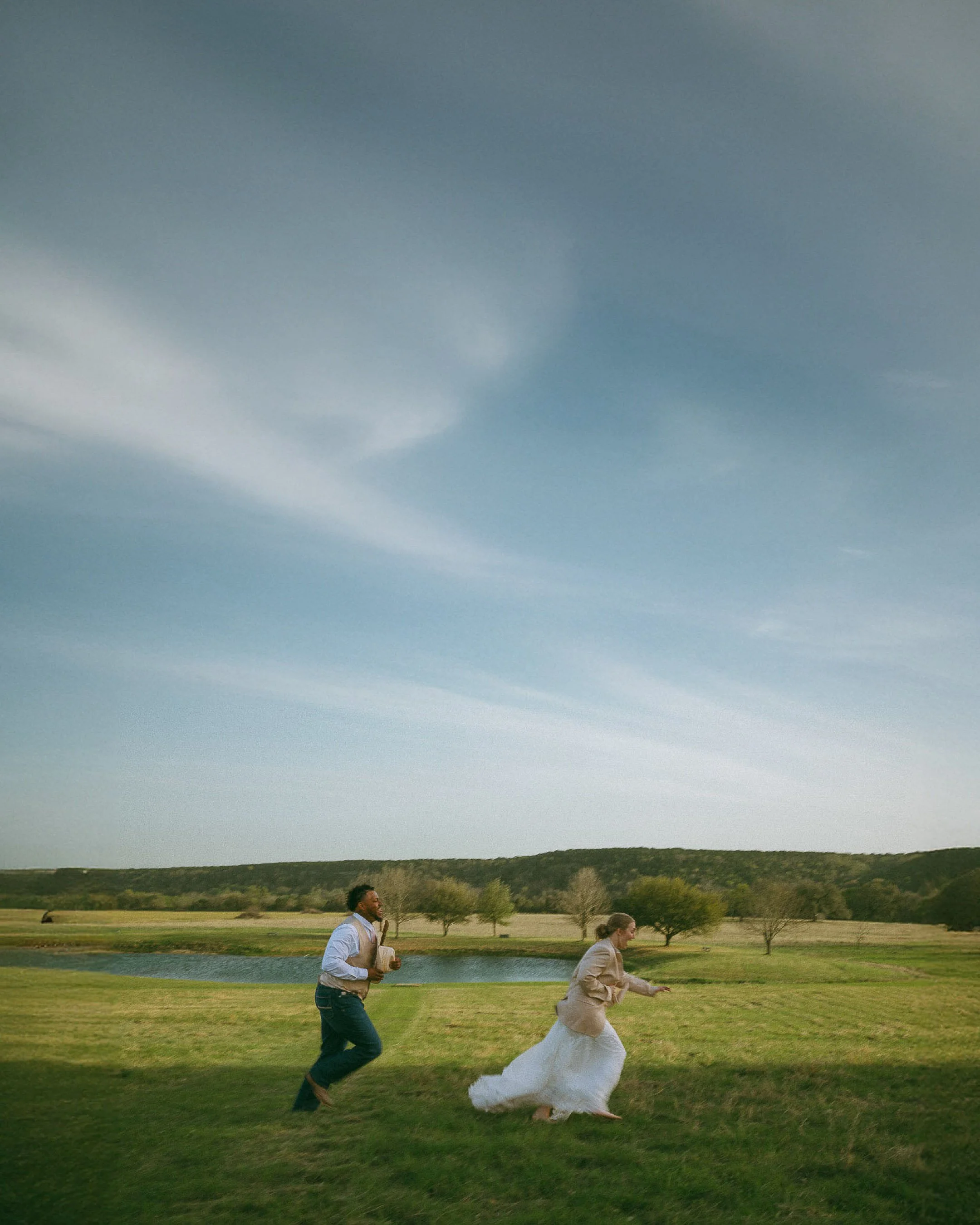 Bride and groom running through a wide open Texas field during cinematic wedding portraits