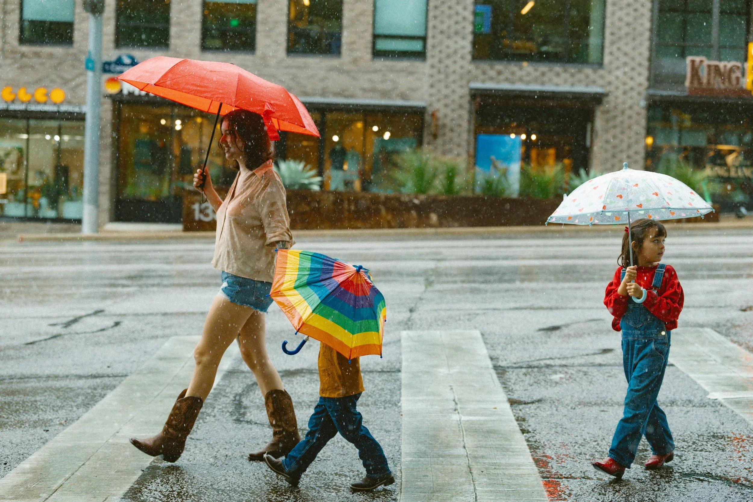 Family in the rain in South Congress, Austin walking across the crosswalk with rainbow umbrellas