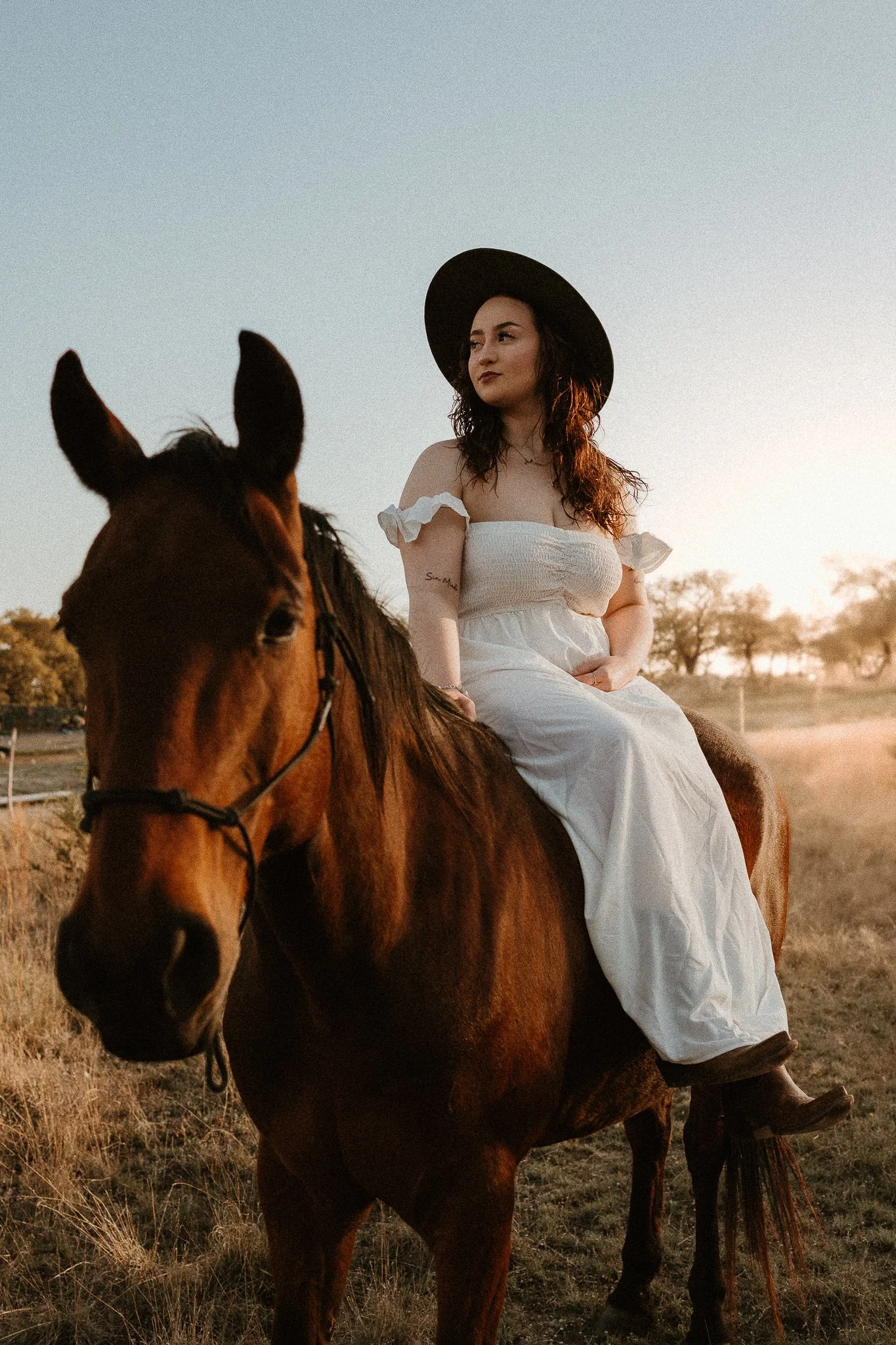 senior sitting on horseback, the sun setting behind them, creating a dreamy Western aesthetic.