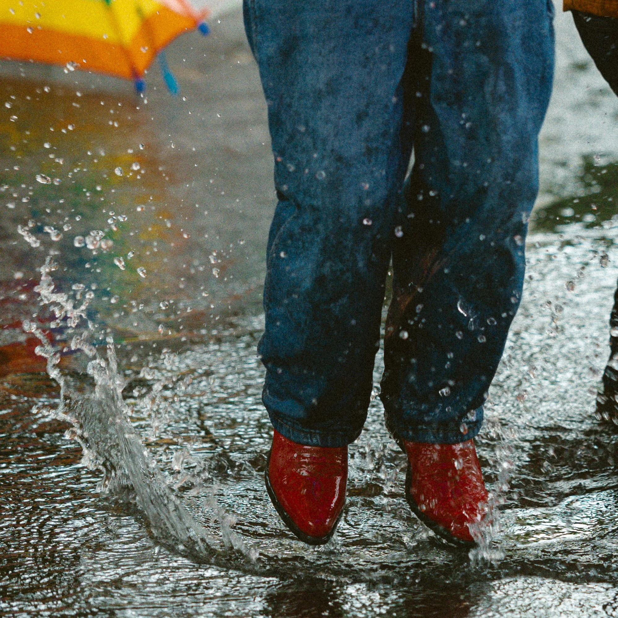 Child in red boots splashing in a puddle in South Congress-Austin, Texas