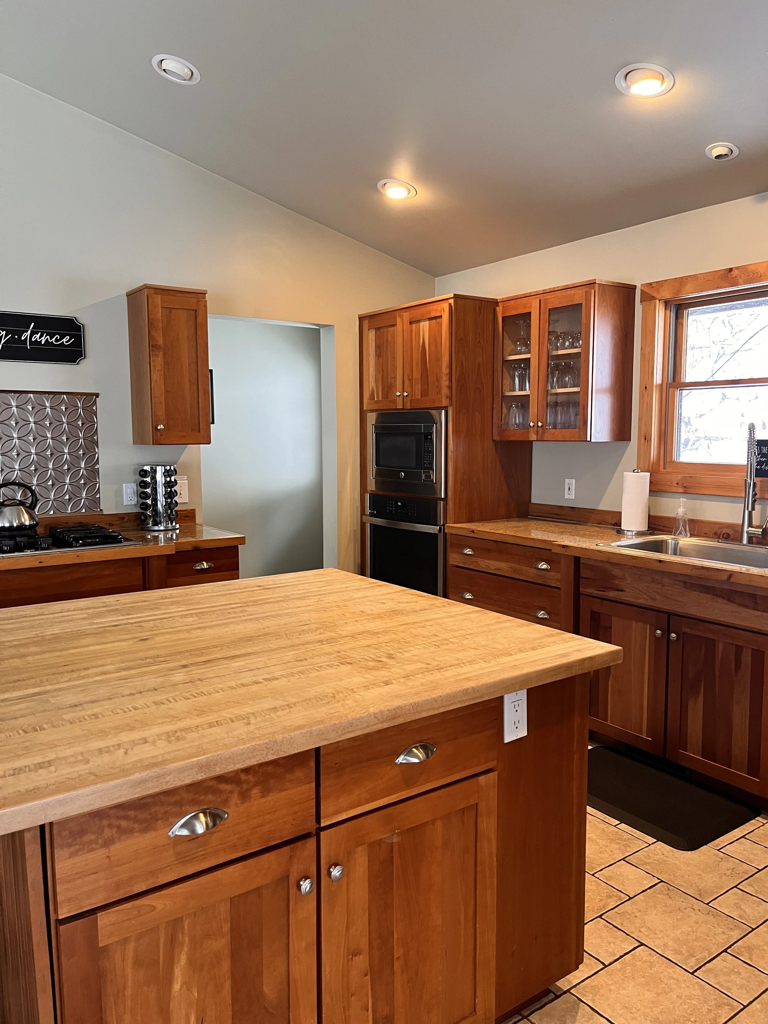 Kitchen with wooden cabinets, a kitchen island with a wood surface, a stove, and a window above the sink.