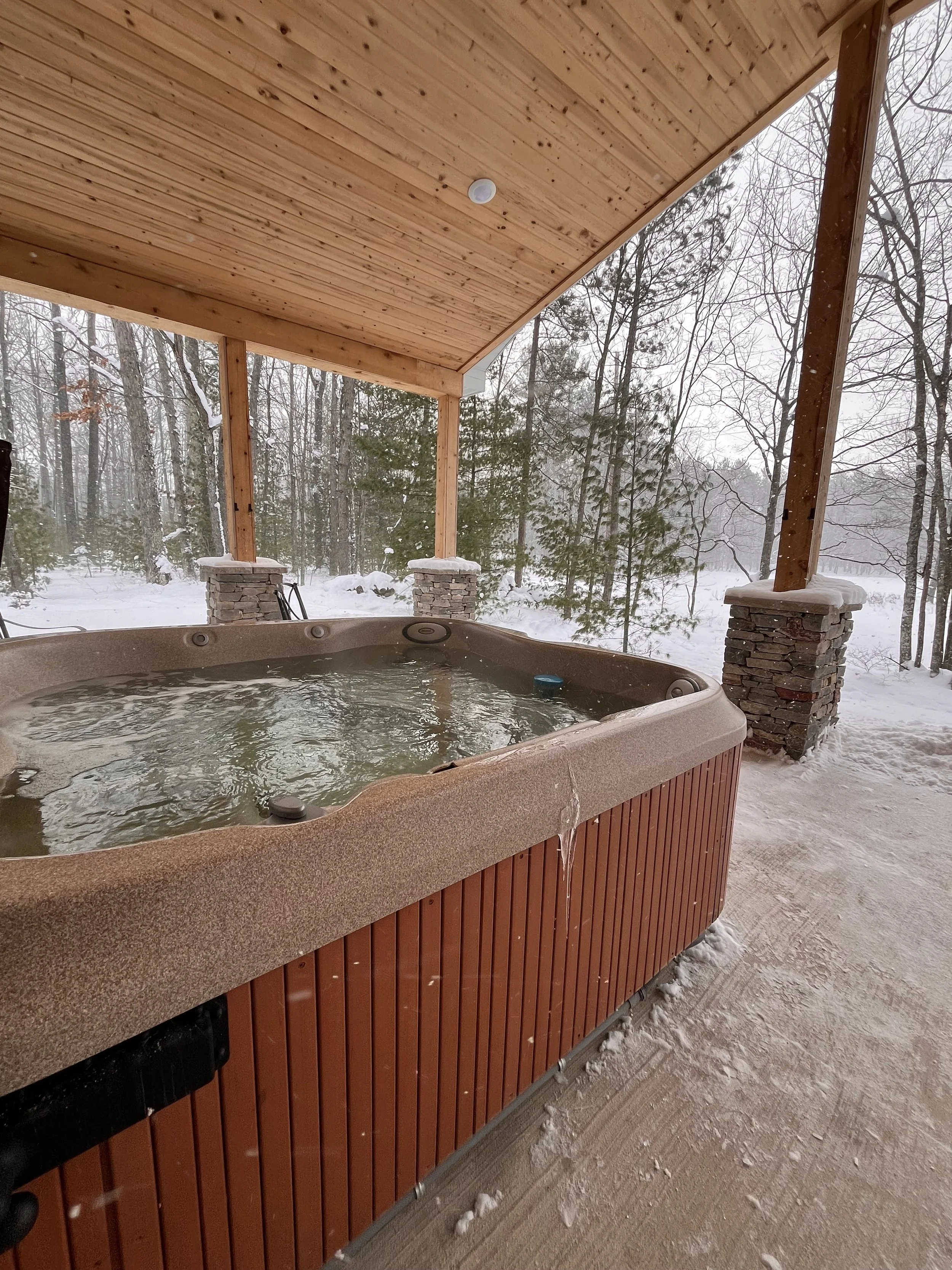 An outdoor hot tub on a wooden porch with a snowy landscape and trees in the background.