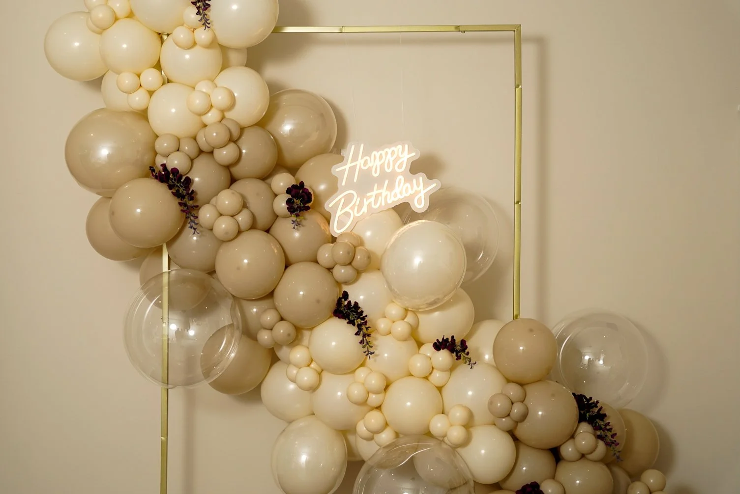 Custom cream organic balloon garland with bubble balloons, purple flowers, and neon "Happy Birthday" sign for birthday parties.