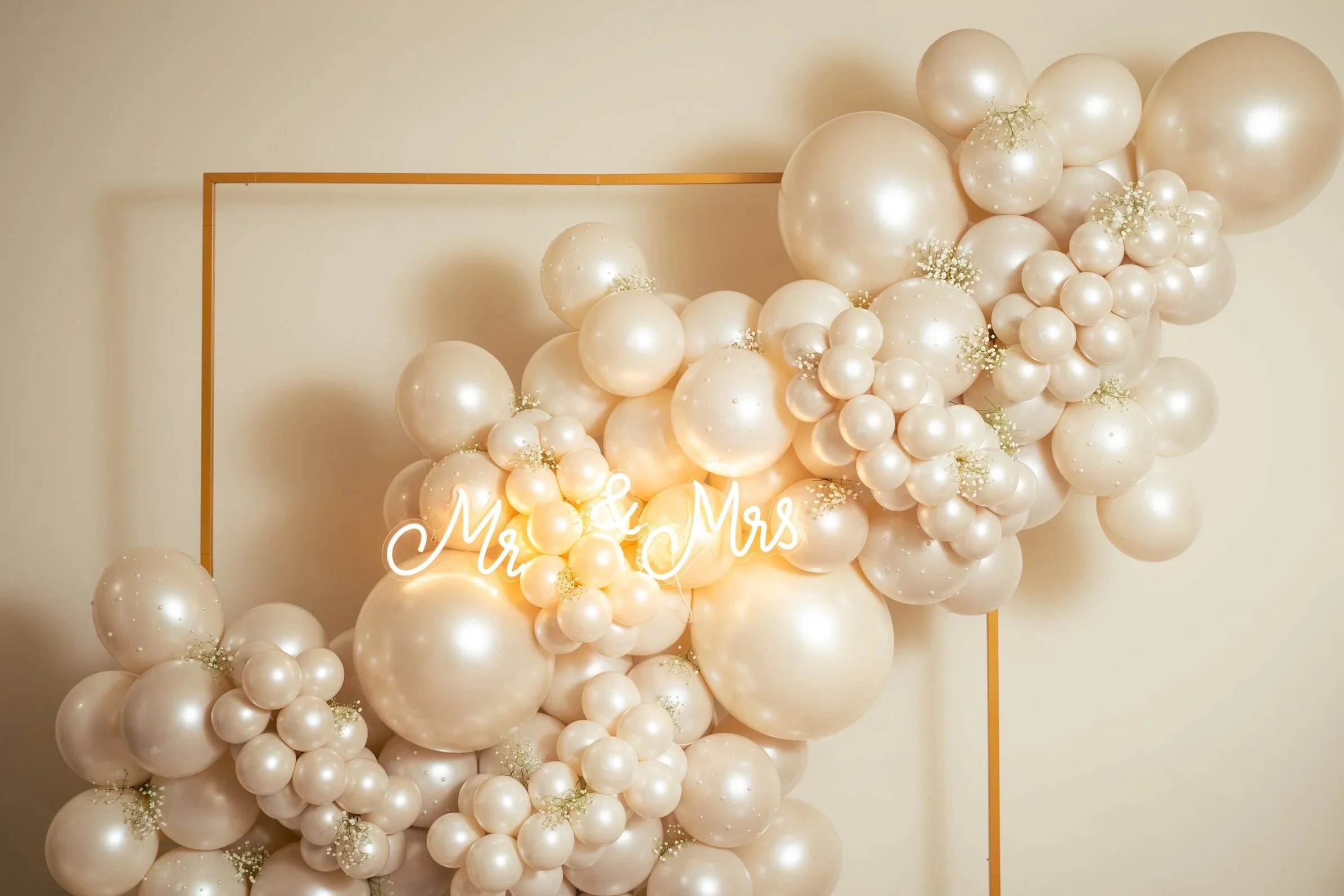 Decorative wedding balloon arrangement with white and pearl-colored balloons, white flowers, and neon sign that reads "Mr. & Mrs." 