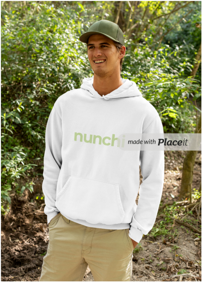 Young man outdoors wearing a white hoodie and khaki pants, smiling, in a forested area with green foliage.