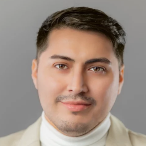 Close-up portrait of a young man with dark hair, light skin, wearing a light-colored suit and white turtleneck, smiling gently against a gray background.