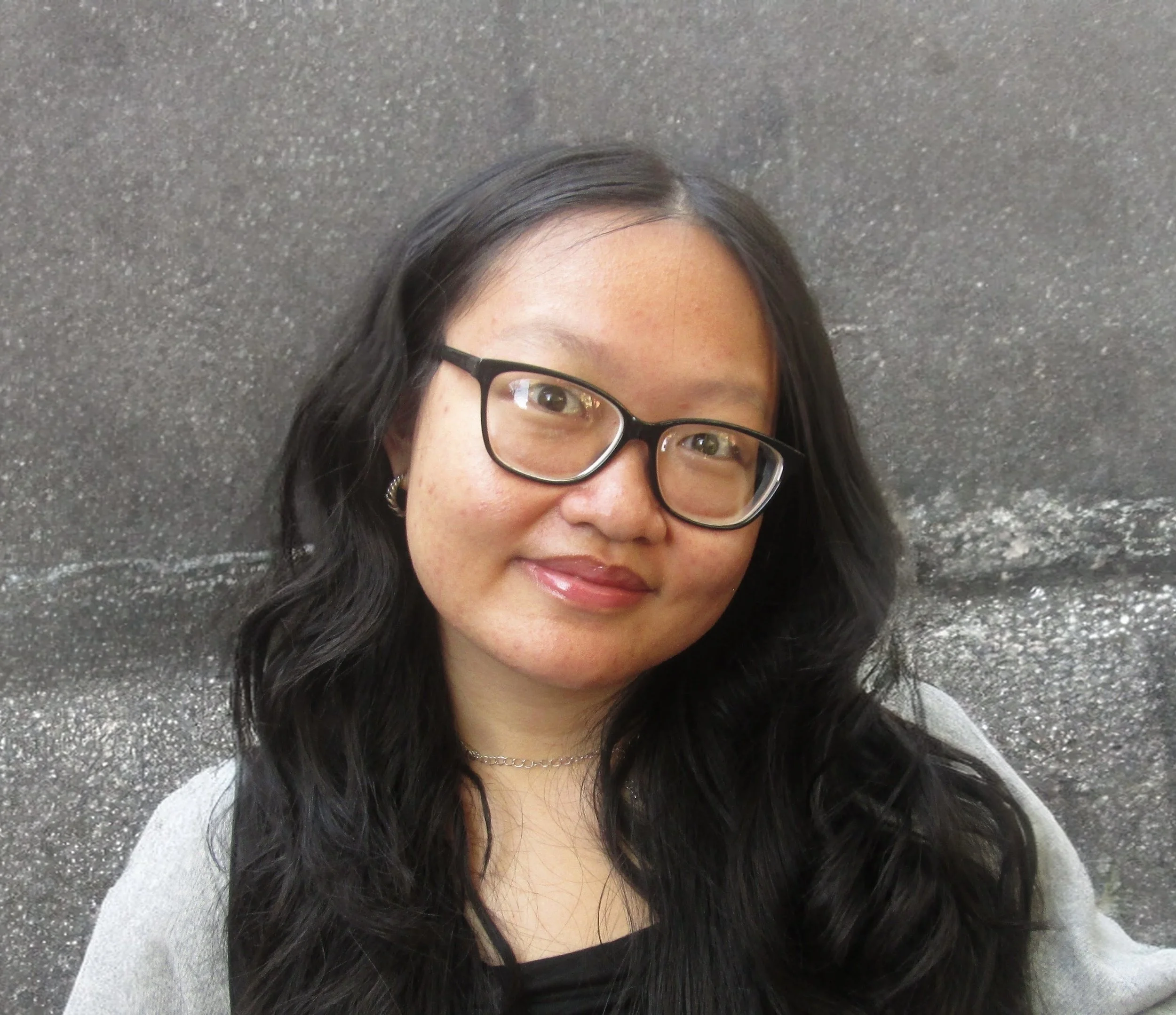 Professional headshot of a young man in a black suit, light blue shirt, and peach tie, smiling against a gray background.
