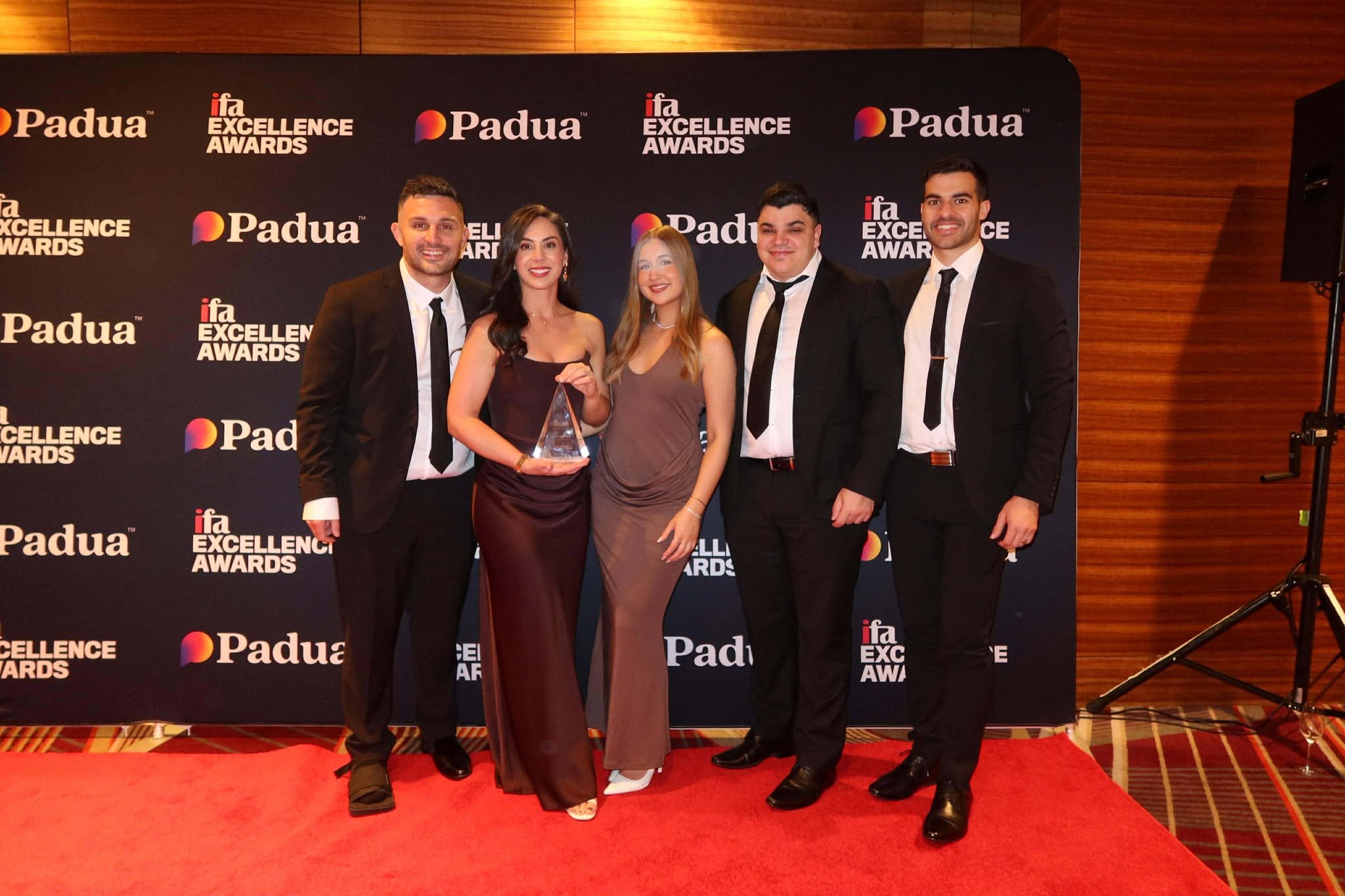 Group of five people in formal attire standing on red carpet at awards event, with a backdrop displaying 'Padua' and 'ifa Excellence Awards' logos.