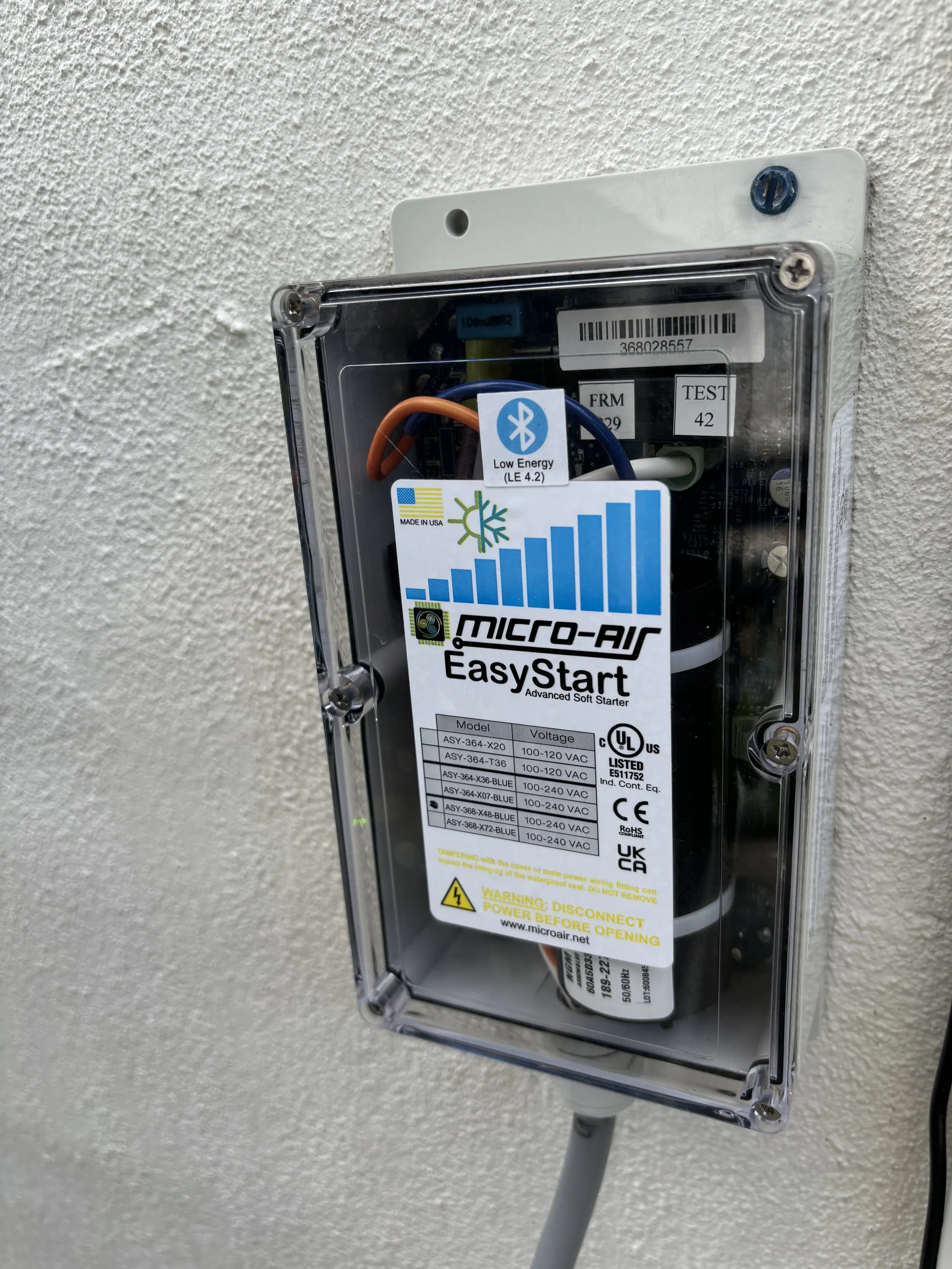 Electrical control box with a label referencing Micro-Air EasyStart soft starter, mounted on a textured white wall.