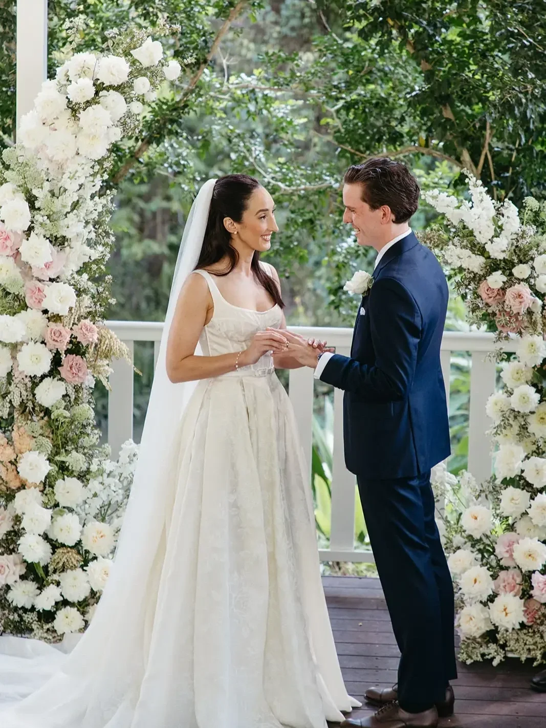 couple smiling at wedding arbour as they say I do with wedding arch florals surrounding them