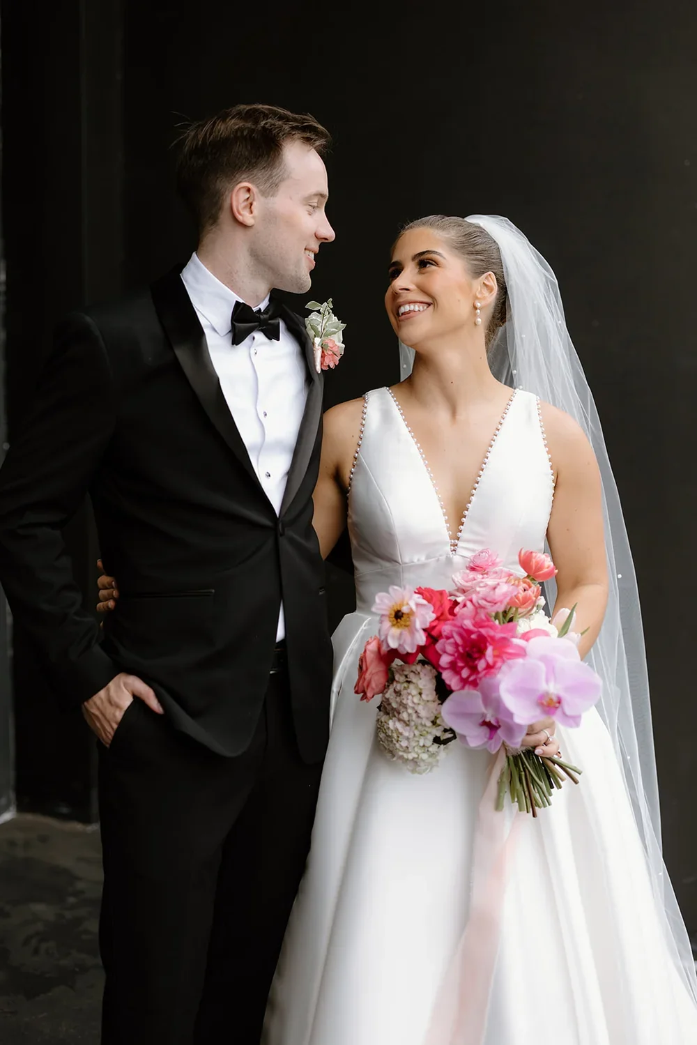 Bridal bouquets with soft peach, blush, hot pink and lavender florals held by bride as she looks into groom's eyes.