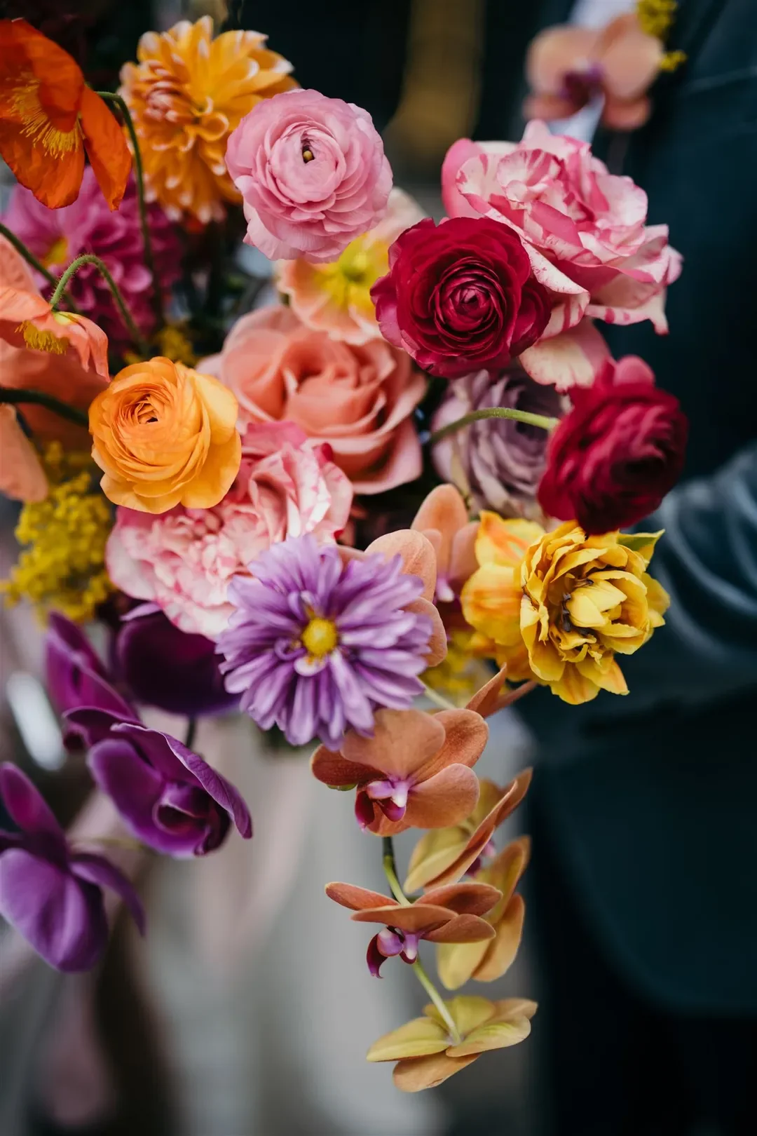 Colourful close-up of Sarah’s vibrant bouquet featuring bold roses, orchids, ranunculus, and dahlias in bright tones.