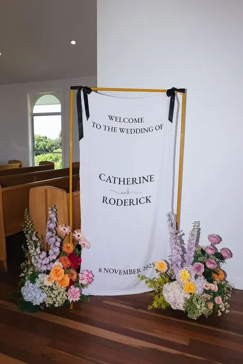Wedding welcome sign framed with colourful Garden Graffiti floral arrangements inside a bright chapel