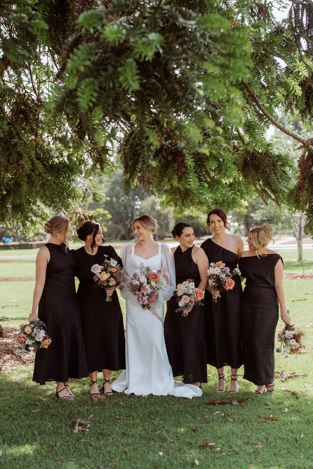 Bridal party standing under lush green foliage holding soft pastel bouquets at Annalise and Mitchell’s outdoor wedding.