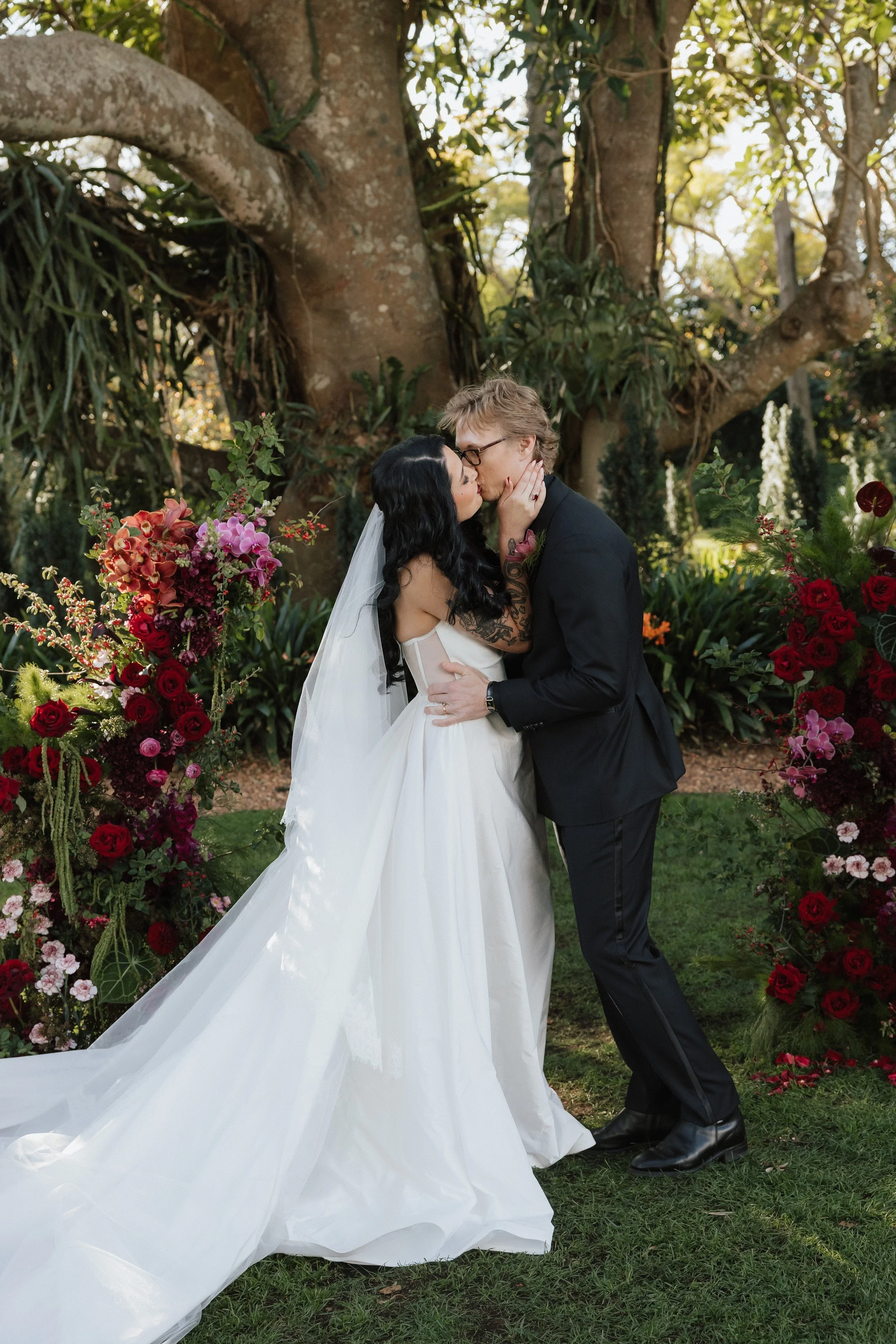 Bride and groom kissing at their Gabbinbar Homestead ceremony in Toowoomba, framed by deep red rose and dahlia installs
