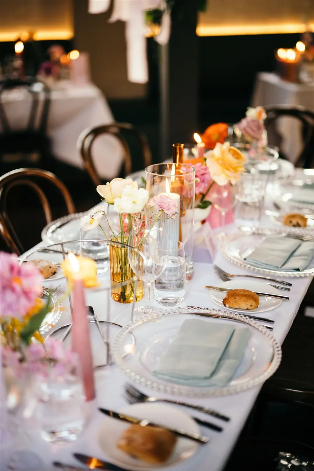 Close-up of elegant table styling with glowing candles and pastel florals in gold bud vases.