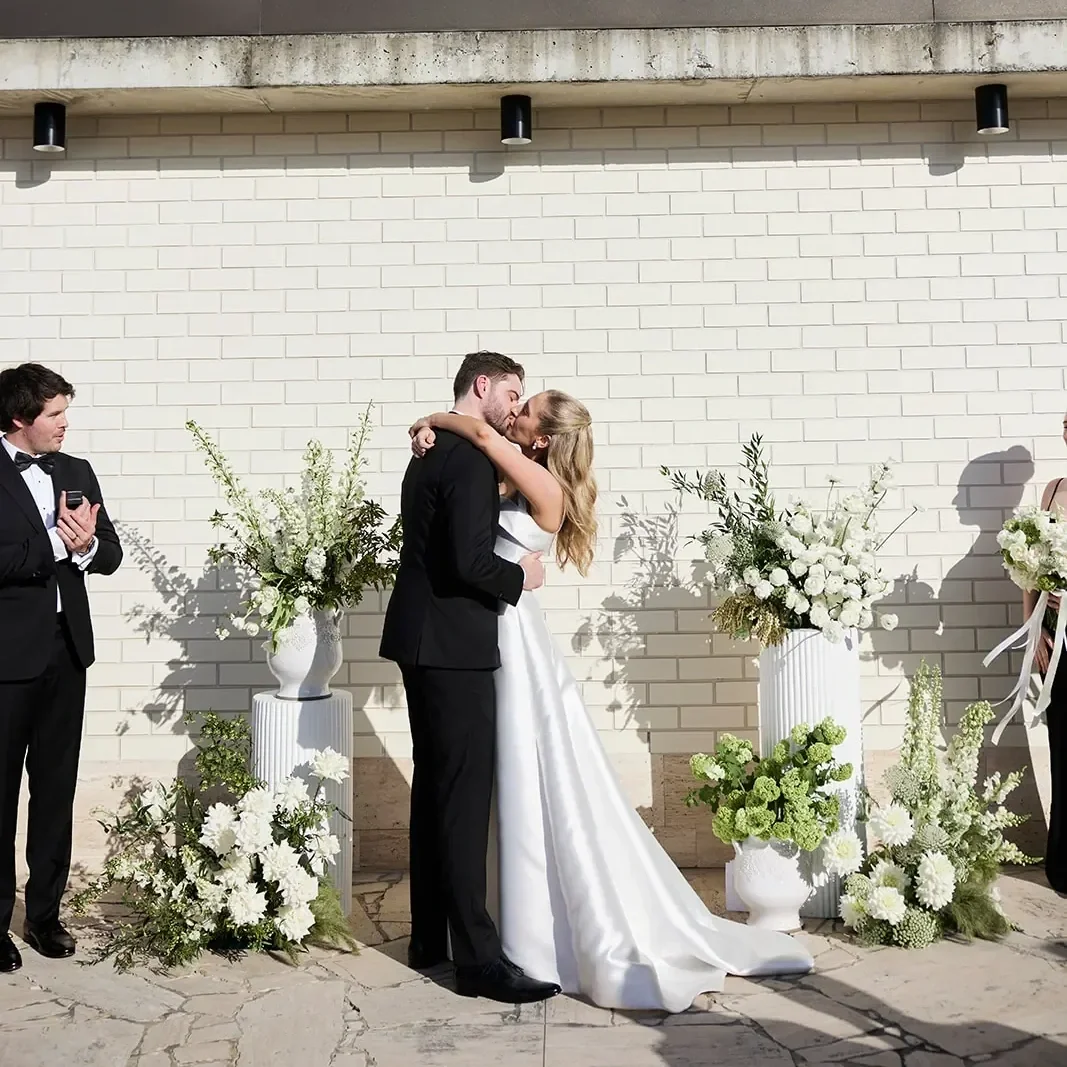 Wedding ceremony kiss framed by large white floral arrangements and plinths designed by a Brisbane wedding florist.