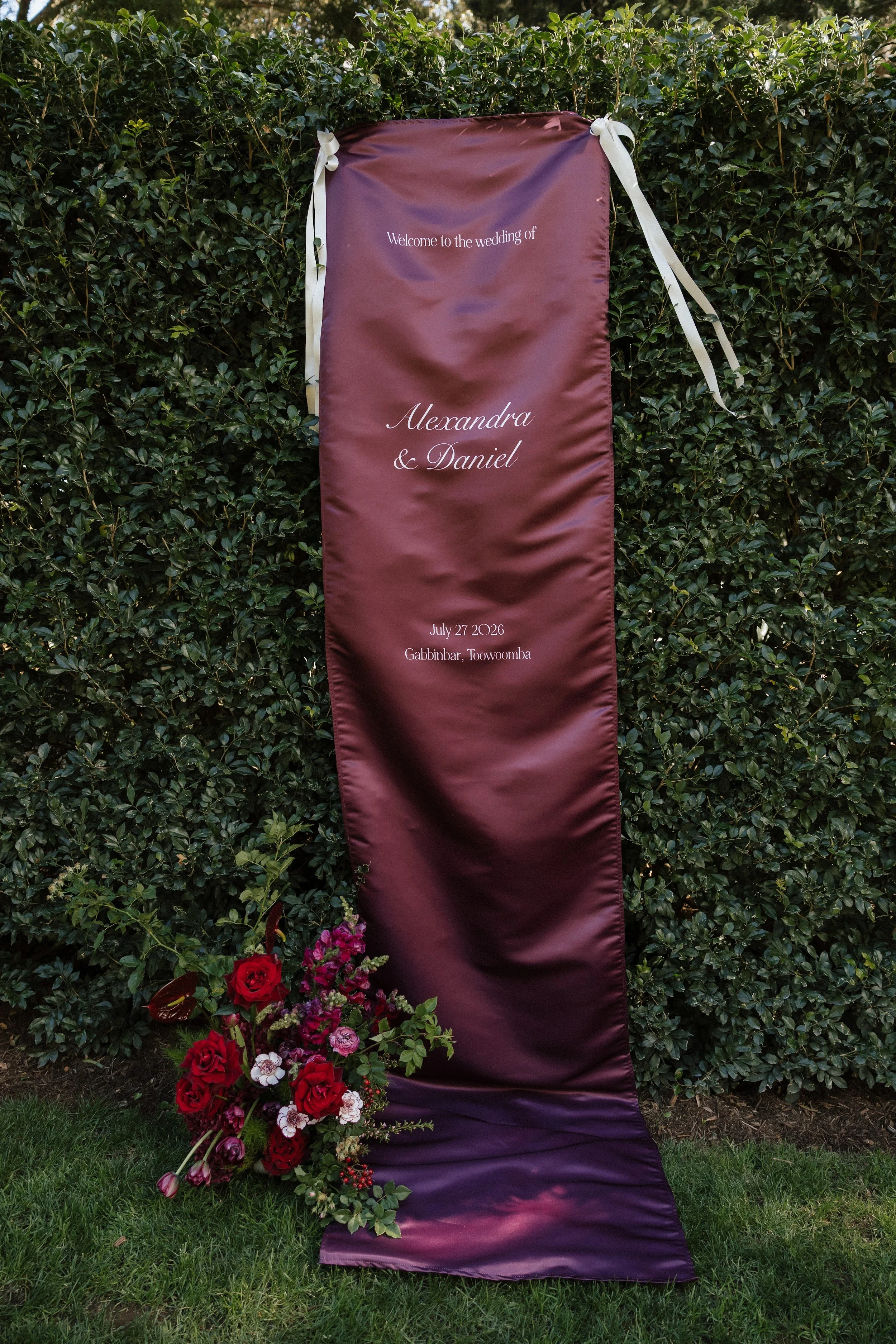 Burgundy draped welcome sign framed by deep red florals at Gabbinbar Homestead