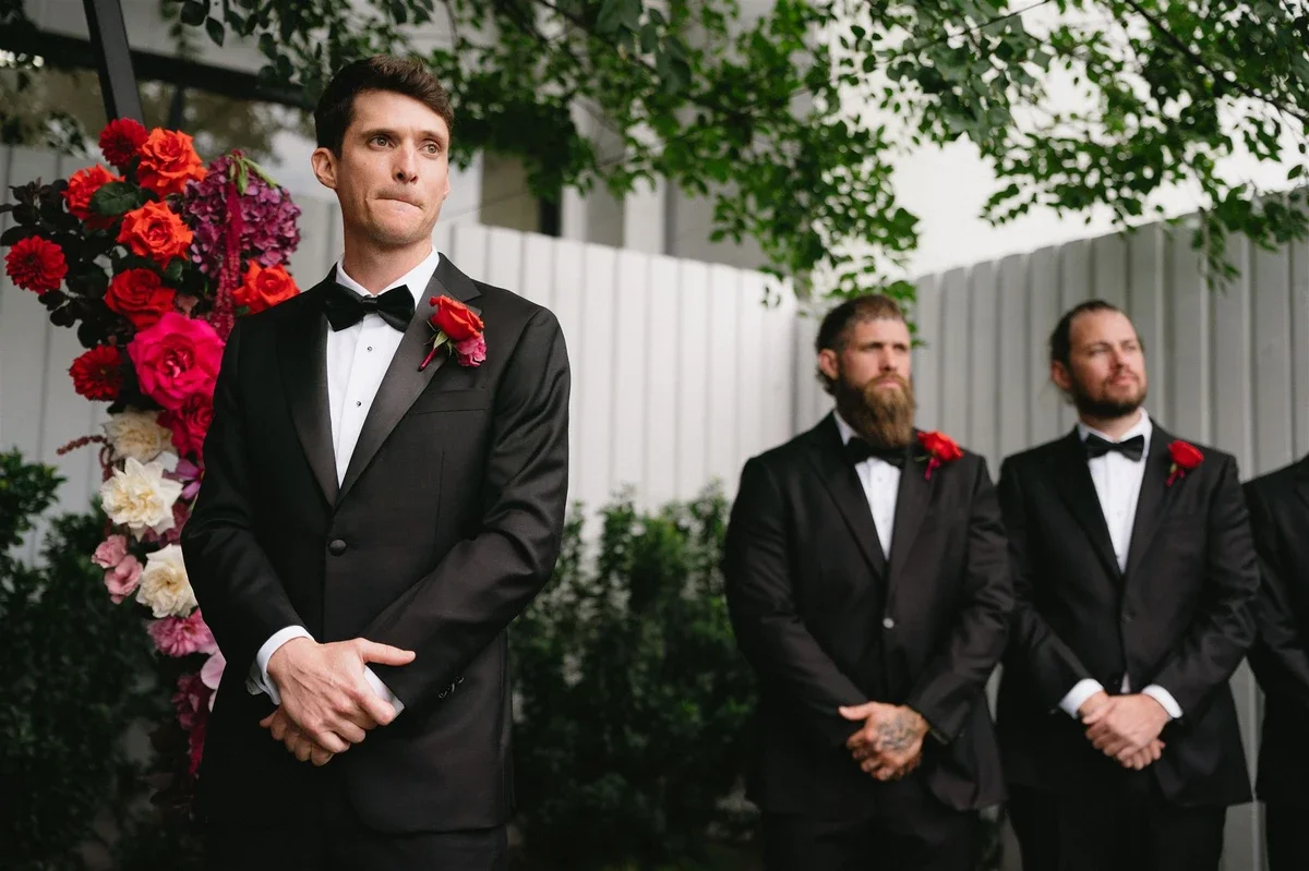 Groom with groomsmen in background looking at bride as she walks down the aisle.