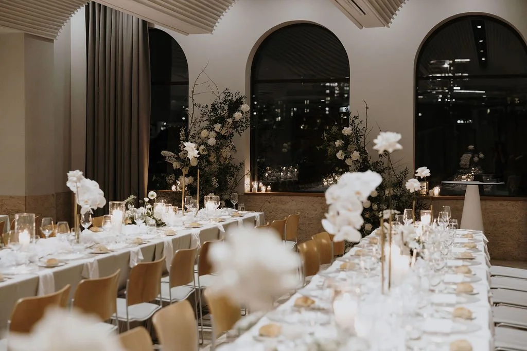 Elegant reception long tables styled with white florals, candles, and modern gold stands.