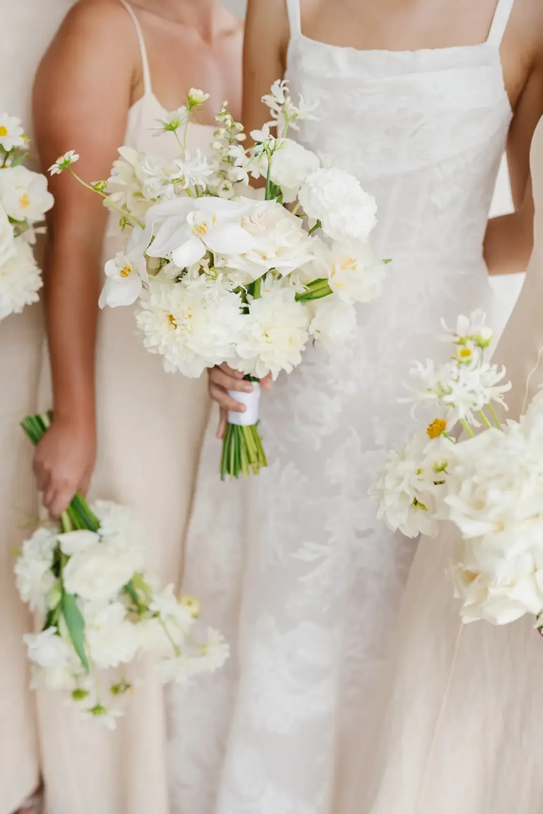 Bridesmaids holding white floral bouquets featuring roses, orchids and seasonal blooms.