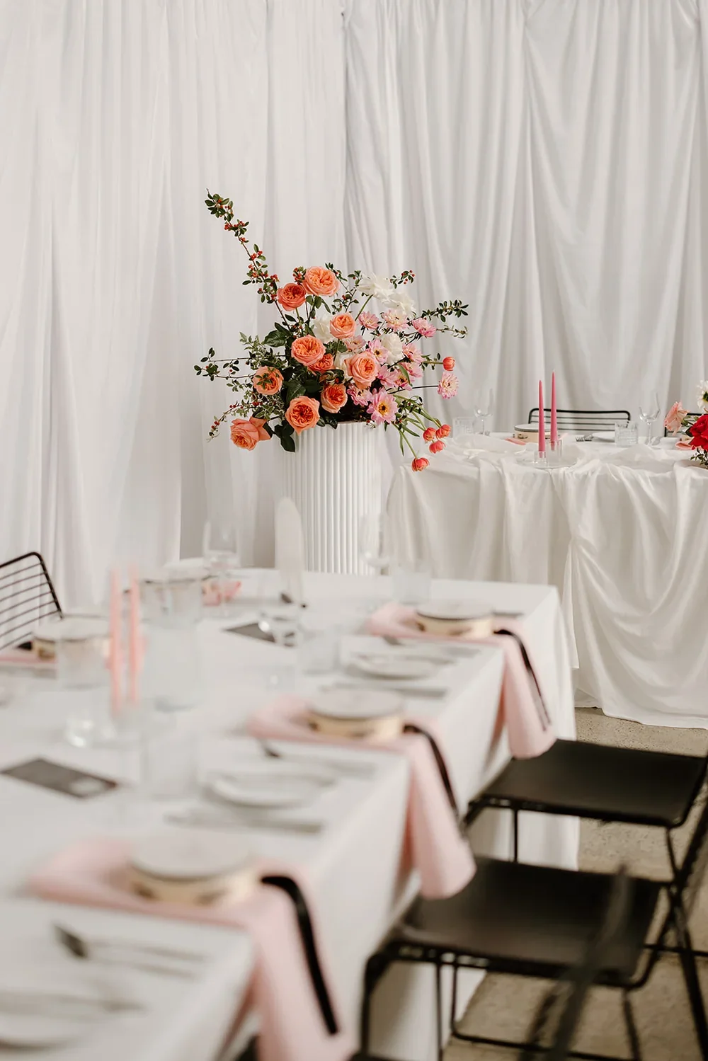 Large statement floral arrangement with peach roses, pink blooms, and greenery displayed in a tall white pedestal vase.