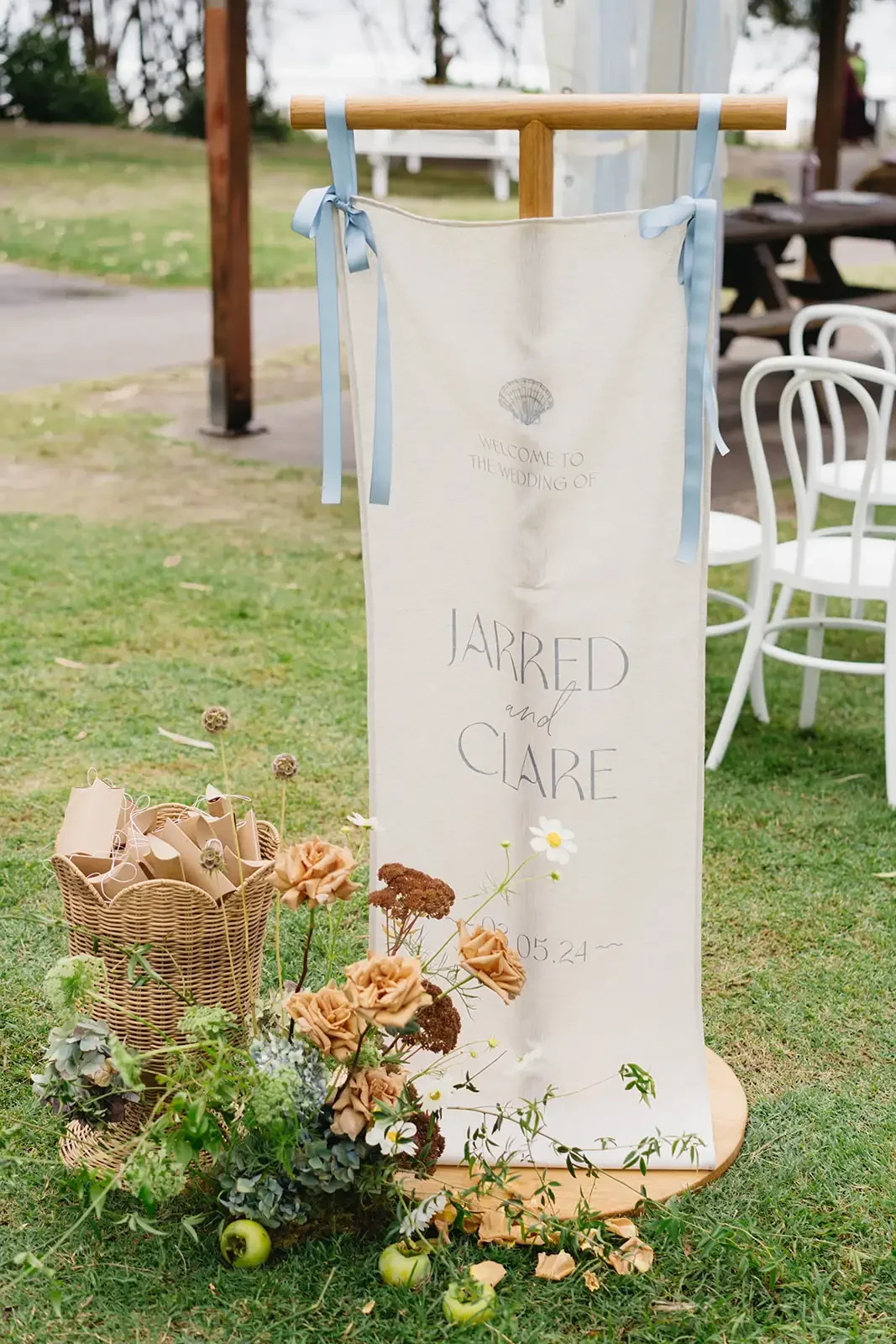 Welcome sign for Clare and Jarred’s wedding styled with warm-toned florals and woven baskets.