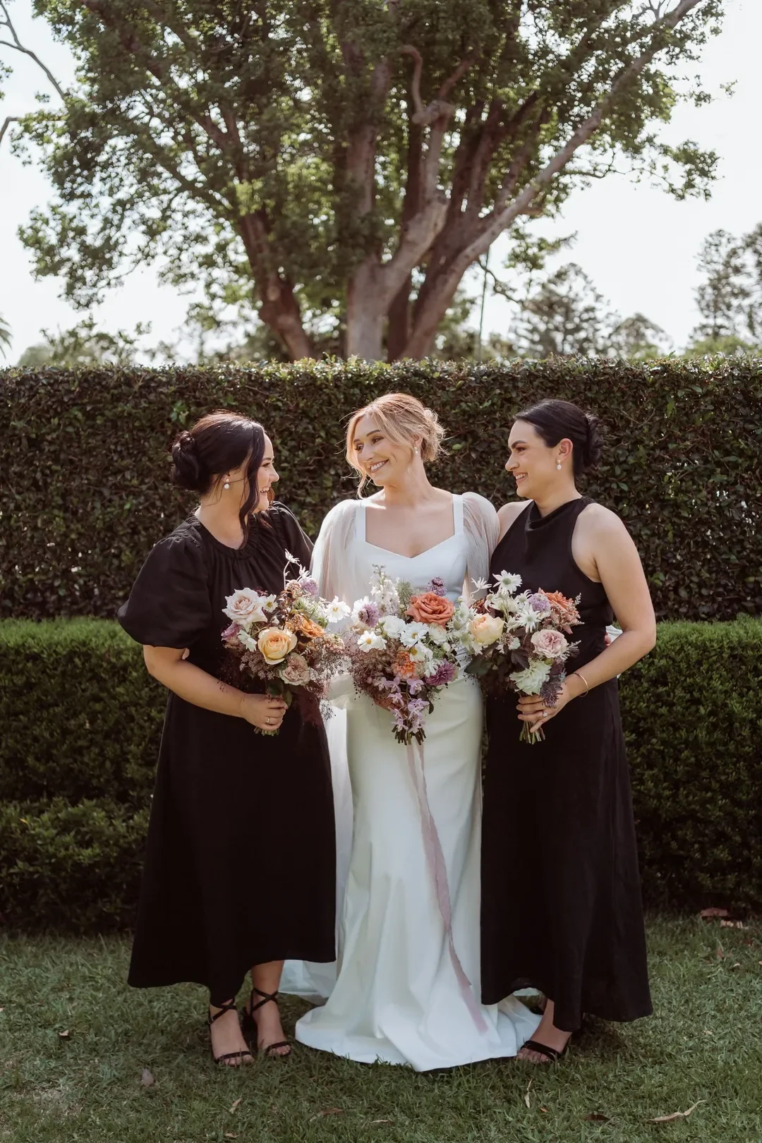 Bride with two bridesmaids smiling together and holding pastel floral bouquets at the wedding.