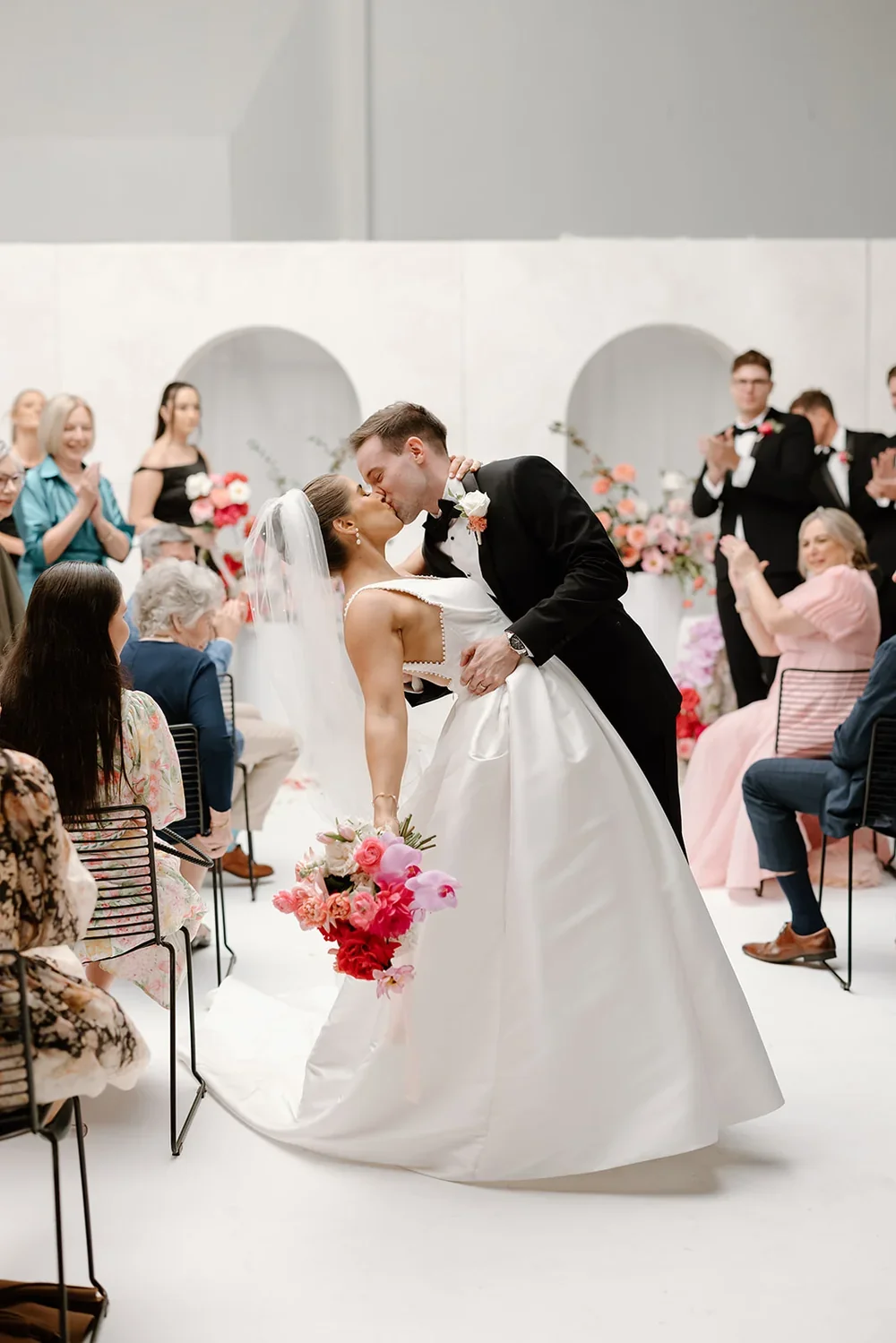 Bride and grooms kissing in aisle with the bride holding a pink and peach floral bouquet
