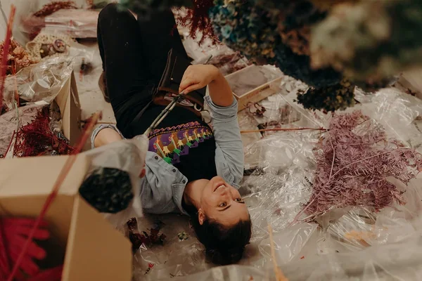 Garden Graffiti team member lying underneath the installation while wiring dried florals into place at West Village.