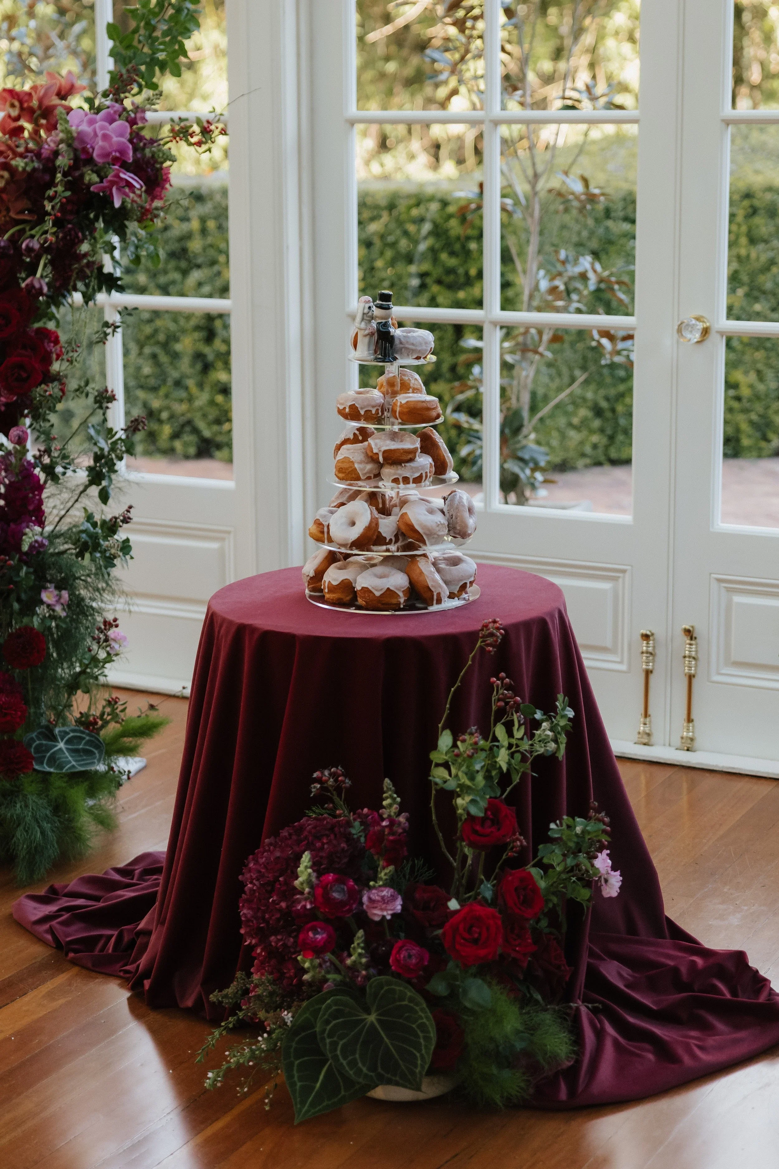 Wedding cake on a burgundy draped table surrounded by deep red florals in the Gabbinbar conservatory