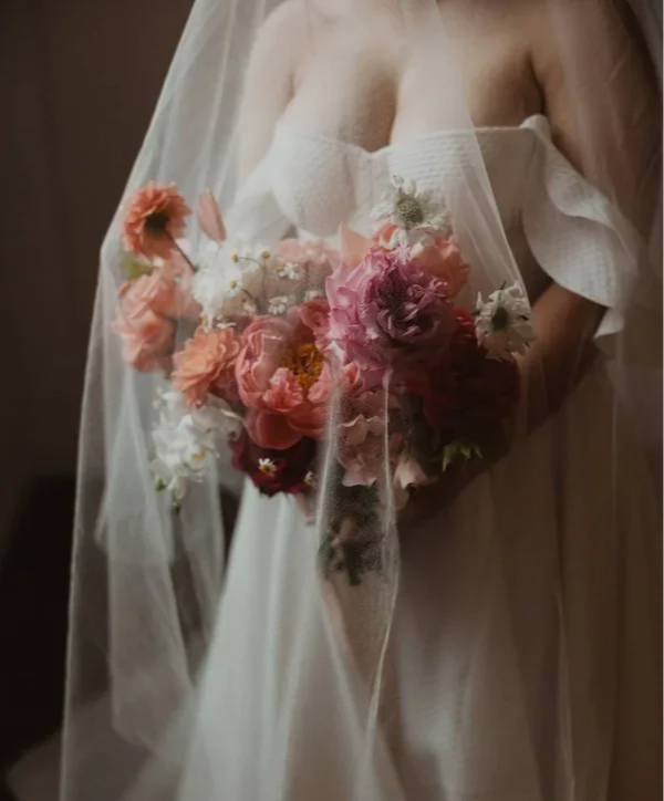 Bridal bouquet in pink, orange and peach tones with a brides' veil floating over the flowers