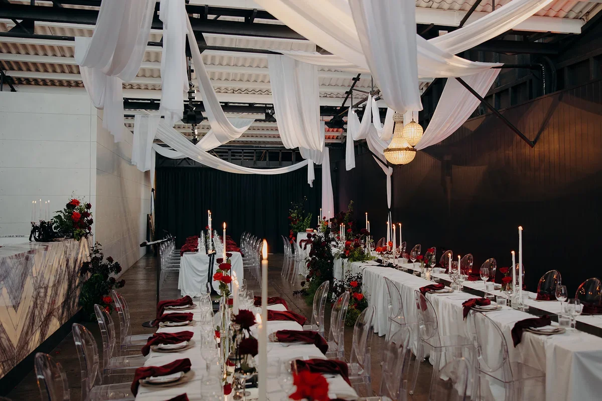 Dramatic reception styling with white drapery from ceiling and red floral accents, candelight and red velvet napkins.
