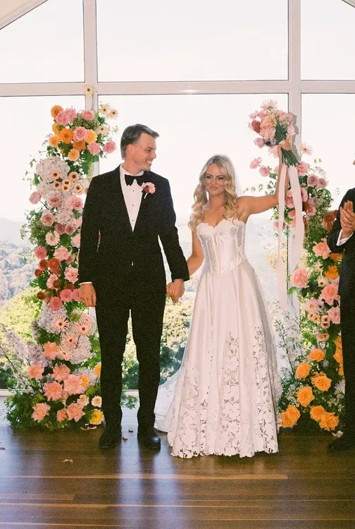 Bride and groom standing beneath floral ceremony pillars, celebrating after their wedding vows