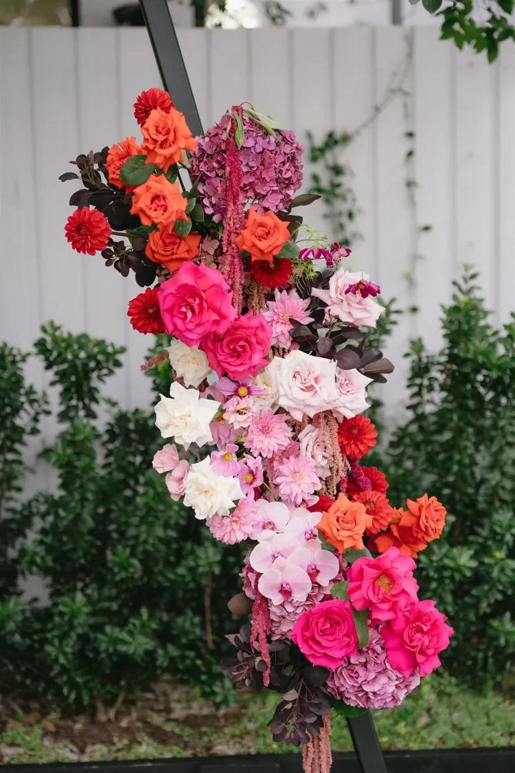 Detailed close-up of vivid pink, peach and orange and red roses and dahlias on the ceremony arbour.