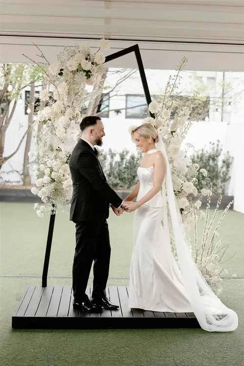 Bride and groom holding hands beneath a modern white floral ceremony installation at The Refinery Brisbane