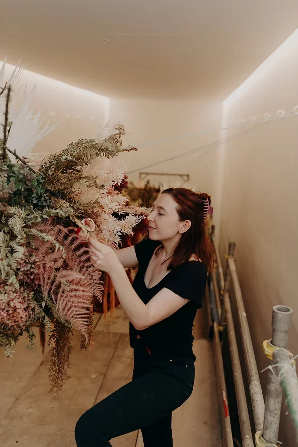 Garden Graffiti florist installing blush and peach-toned dried florals on the large hanging structure at West Village.