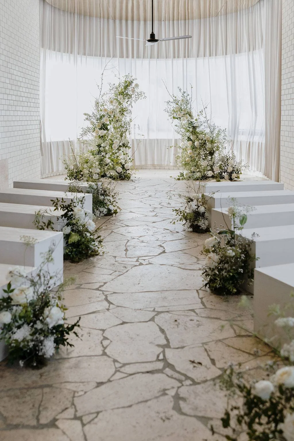 Green and white floral down wedding aisle with two tall floral arrangements facing toward each other
