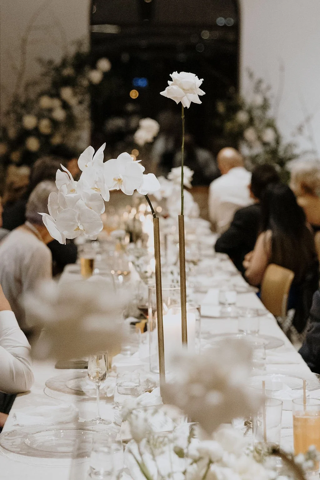 Reception table with tall white orchid stems, candles, and soft romantic floral styling.