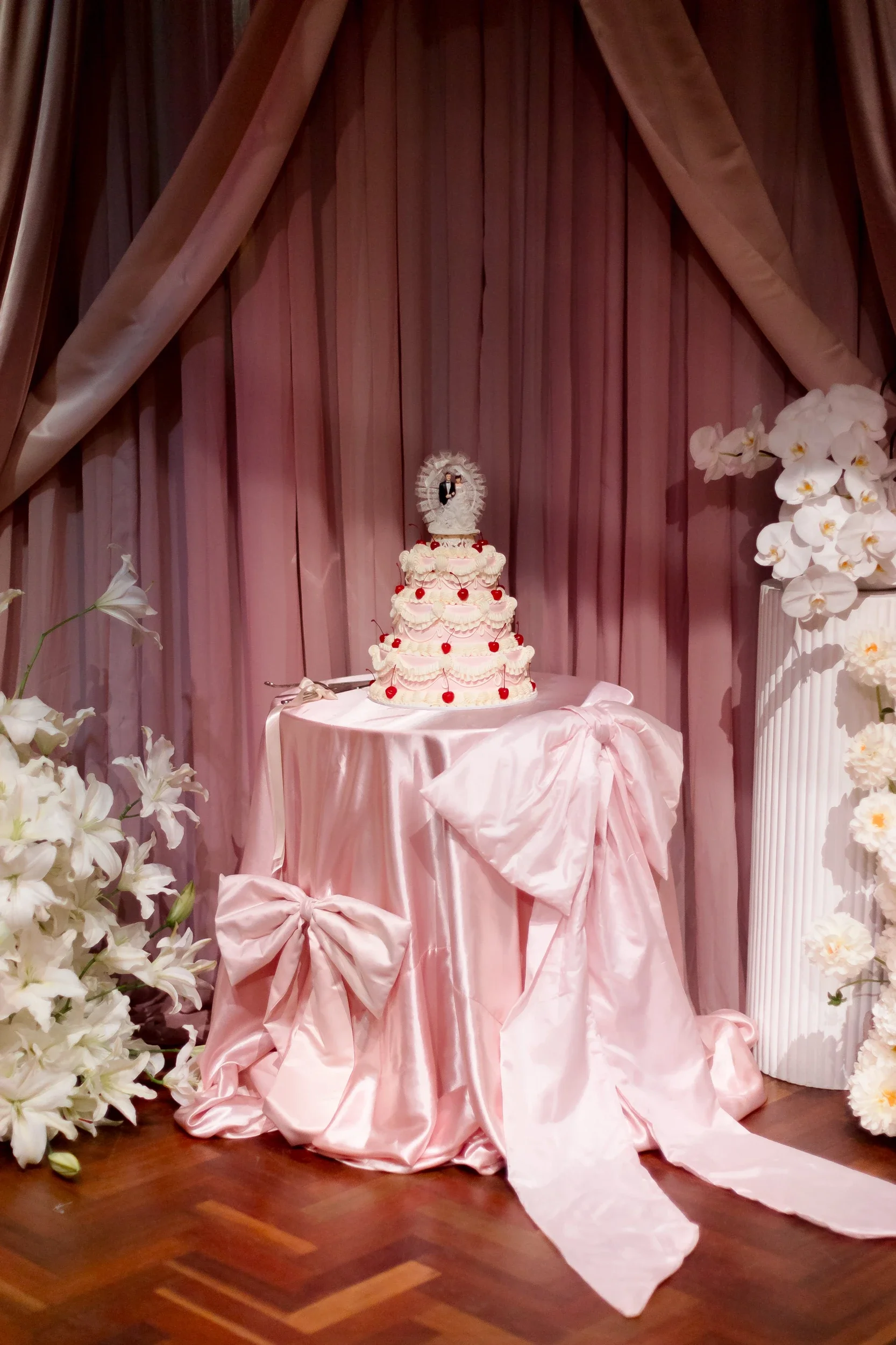 Tiered wedding cake on a pink satin draped table surrounded by white florals